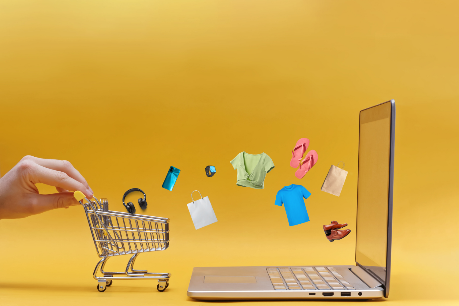 Carrinho de compras em miniatura ao lado de um notebook, com ícones de produtos de e-commerce como roupas, calçados e eletrônicos saindo da tela.